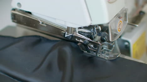 Close-up-the-overstitching-machine-passes-the-edges-of-the-black-fabric-in-slow-motion.-Serger-process-in-the-sewing-workshop